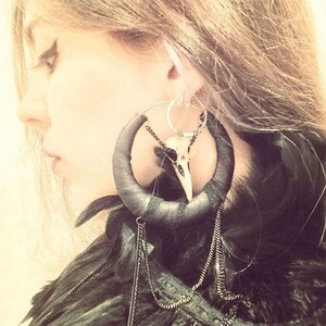 May include: Large black hoop earrings with a bird skull charm and feather accents. The earrings are made of leather and have a silver hoop.