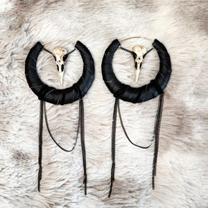 May include: A pair of black leather hoop earrings with a dangling chain and a small white bird skull charm.