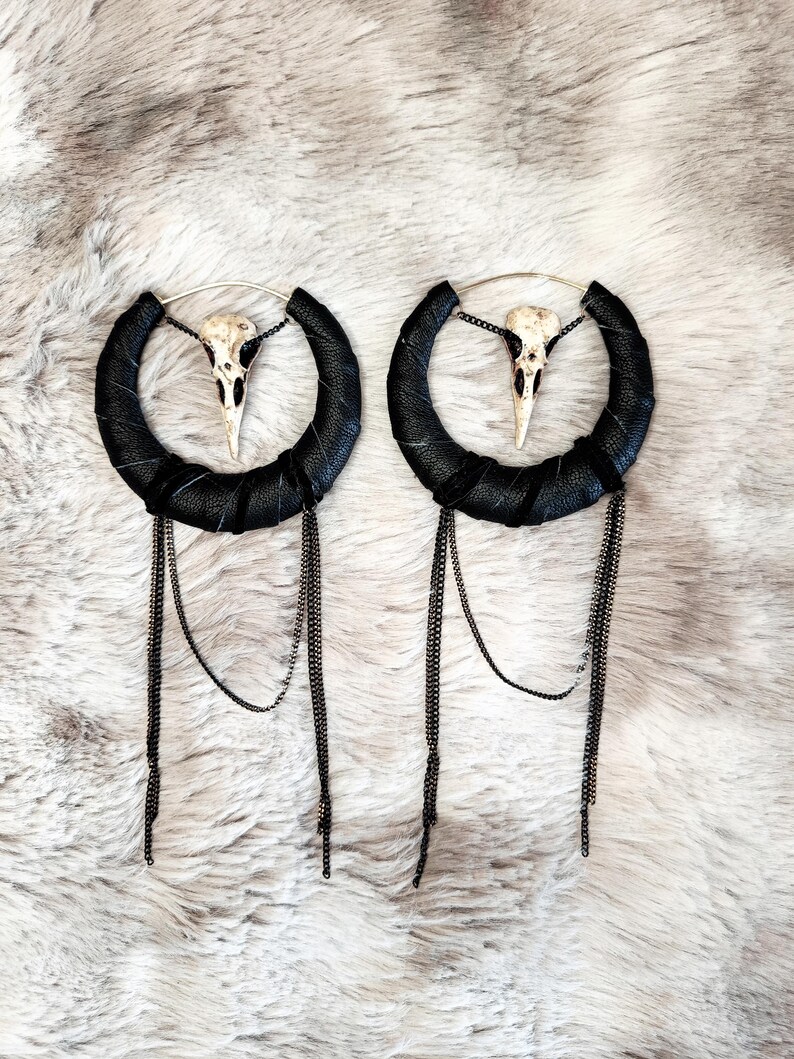 May include: A pair of black leather hoop earrings with a dangling chain and a small white bird skull charm.