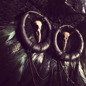 May include: A pair of black leather hoop earrings with dangling chains and a small white skull charm on each hoop.