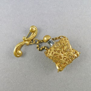 May include: A gold-toned filigree perfume bottle with a clear glass vial and a chain attached to a decorative pin.