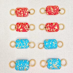 May include: Six rectangular jewelry components. Two sets of three components each. The first set has a red background with gold flecks. The second set has a turquoise background with gold flecks. Each component has gold rings on each end.