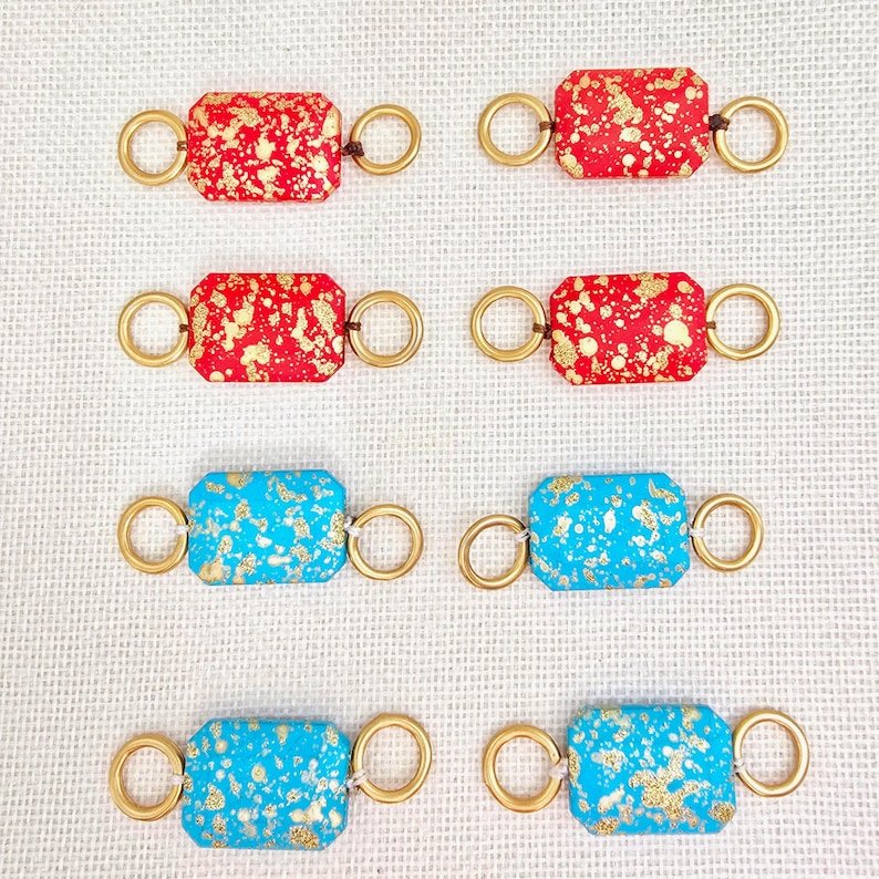 May include: Six rectangular jewelry components. Two sets of three components each. The first set has a red background with gold flecks. The second set has a turquoise background with gold flecks. Each component has gold rings on each end.