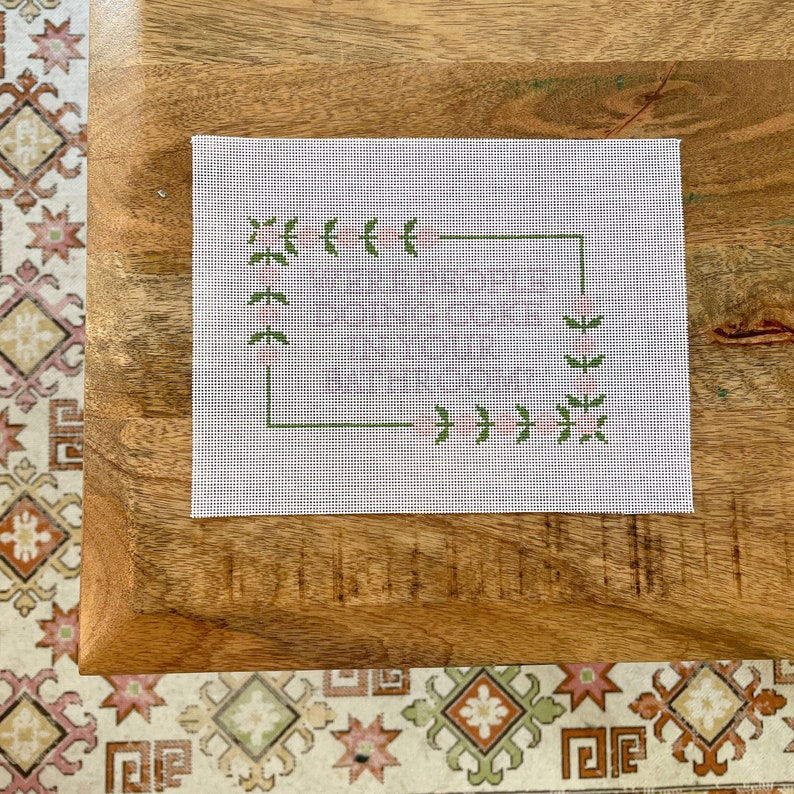 Puede incluir: Un lienzo blanco con un borde floral verde y rosa. El lienzo est&aacute; listo para el bordado.