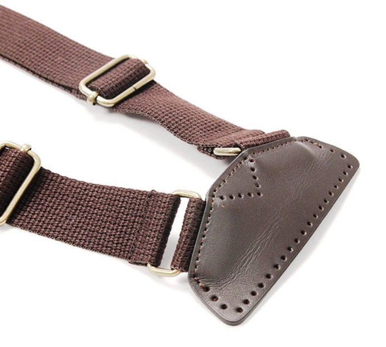 May include: Brown canvas strap with a leather patch and gold metal hardware. The strap has a stitched design on the leather patch.