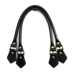 May include: Black leather handbag handles with gold metal hardware and decorative stitching.