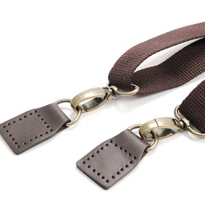 May include: Two brown leather straps with brass clasps and metal rings. The straps are connected to each other with the clasps.
