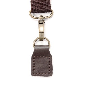 May include: A brown leather strap with a metal clasp and a brown leather loop. The strap is attached to a metal ring.