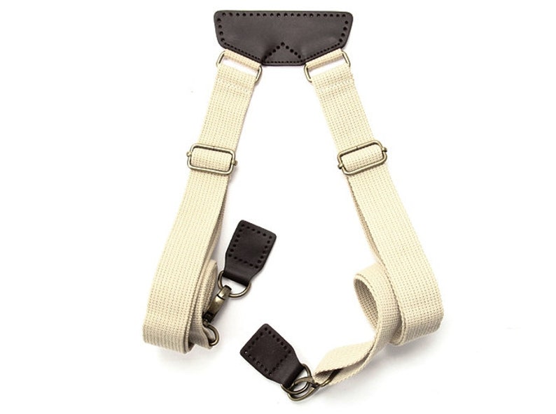 May include: A pair of beige canvas shoulder straps with brown leather accents and metal hardware. The straps are adjustable and can be used to carry a bag or other item.
