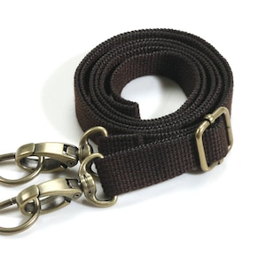 May include: A brown canvas strap with two gold metal clasps. The strap is adjustable and can be used for a variety of purposes.