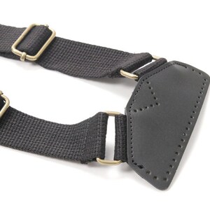 May include: Black canvas strap with two gold metal buckles and a black leather patch with stitching.