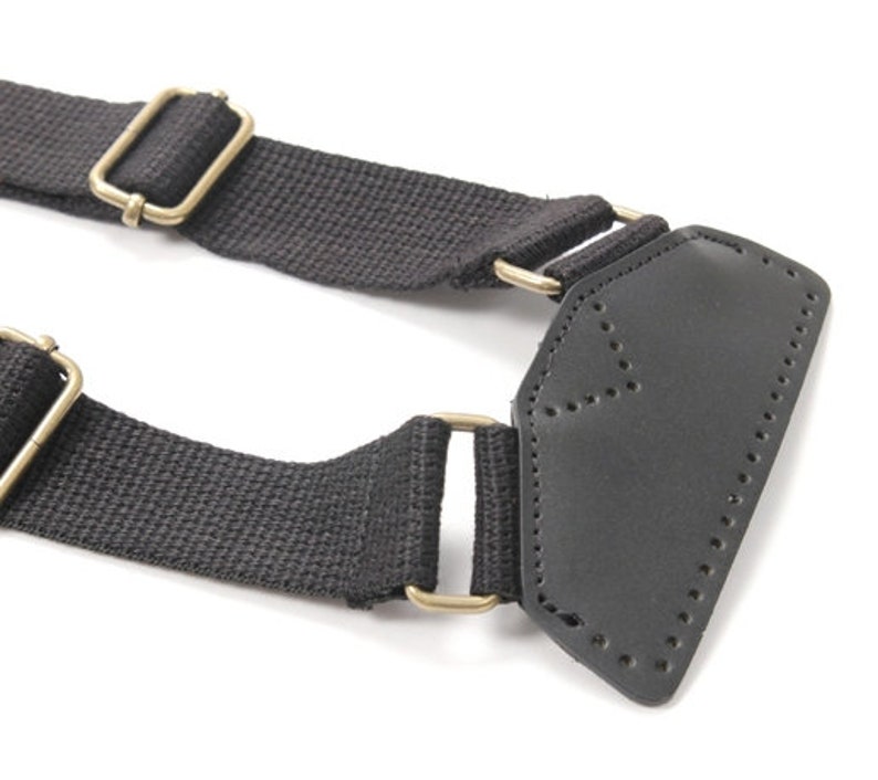 May include: Black canvas strap with two gold metal buckles and a black leather patch with stitching.