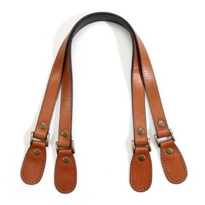 May include: A pair of brown leather handles with metal buckles and rivets. The handles are designed to be attached to a bag or purse.