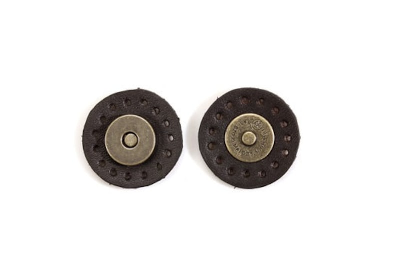 May include: Two brown leather magnetic closures with metal snaps. The snaps have the text "GOOD LUCK" and "MADE IN ITALY" on them.