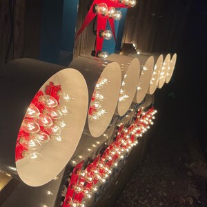 K&ouml;nnte beinhalten: Nahaufnahme eines Vintage-Schilds mit wei&szlig;en runden Lichtern und roten Akzenten. Die Lichter sind in einer Reihe angeordnet und leuchten, wodurch ein warmes Leuchten entsteht.