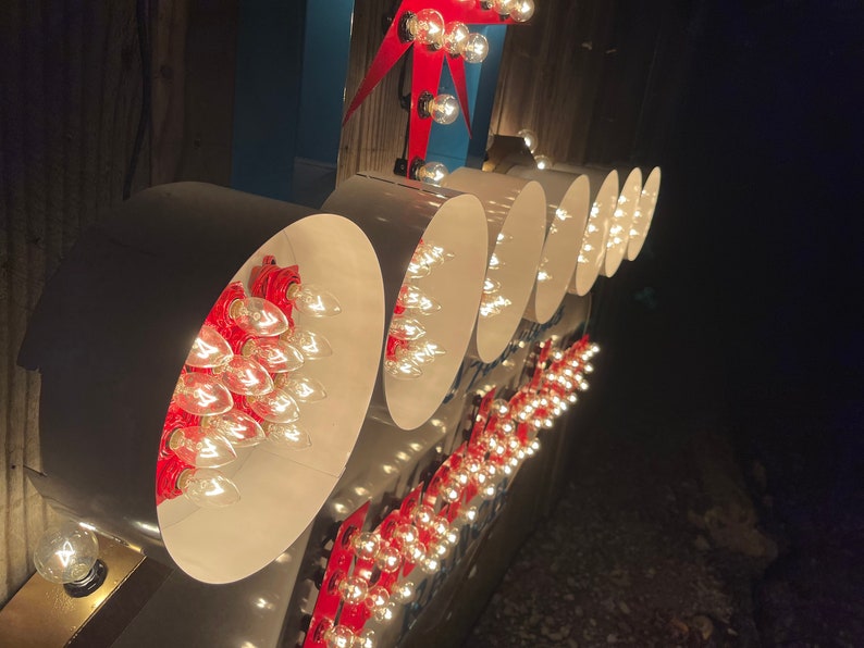 K&ouml;nnte beinhalten: Nahaufnahme eines Vintage-Schilds mit wei&szlig;en runden Lichtern und roten Akzenten. Die Lichter sind in einer Reihe angeordnet und leuchten, wodurch ein warmes Leuchten entsteht.