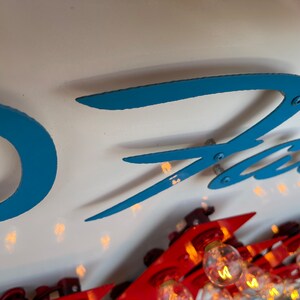 K&ouml;nnte beinhalten: Nahaufnahme eines blauen und wei&szlig;en Schilds mit dem Wort "Fast" in einer stilisierten Schrift. Das Schild hat mehrere kleine, runde, silberne Lichter an den R&auml;ndern.