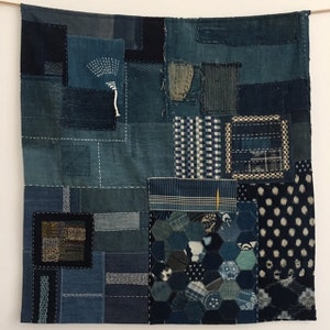 May include: A patchwork quilt made of various shades of blue denim fabric. The quilt is made up of different sized squares and rectangles, some of which have been stitched together with decorative stitching. The quilt is a beautiful example of traditional Japanese textile art.