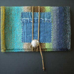 Puede incluir: Una bolsa de tejido tejido con un parche de mezclilla azul y un cierre de concho plateado. La bolsa está atada con cordones de cuero marrón.