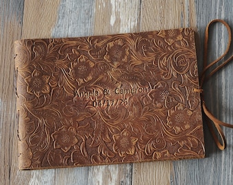 May include: A brown leather-bound journal with a floral embossed design. The journal has a leather tie closure and is personalized with the names "Angela & Cameron" and the date "04/17/2026".