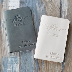May include: Two leather-bound vow books, one gray and one white, with the words "His Vows" and "Her Vows" embossed on the front. The books are personalized with names and dates.