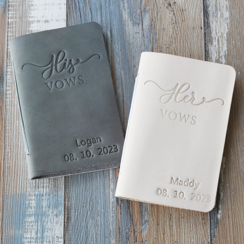 May include: Two leather-bound vow books, one gray and one white, with the words "His Vows" and "Her Vows" embossed on the front. The books are personalized with names and dates.