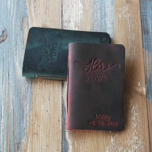 May include: Two leather-bound journals with the words "His Vows" and "Her Vows" embossed on the covers. The journal on the right has the date "08.10.2023" and the name "Maddy" embossed on the cover.