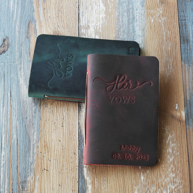 May include: Two leather-bound journals with the words "His Vows" and "Her Vows" embossed on the covers. The journal on the right has the date "08.10.2023" and the name "Maddy" embossed on the cover.