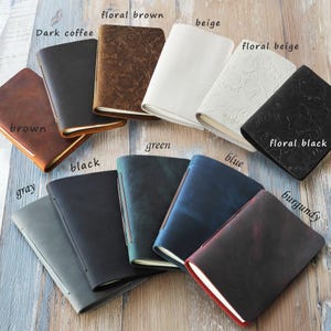 May include: A collection of leather journals in various colors, including brown, black, gray, green, and blue. Some journals feature embossed floral patterns. The journals are open, revealing the pages.