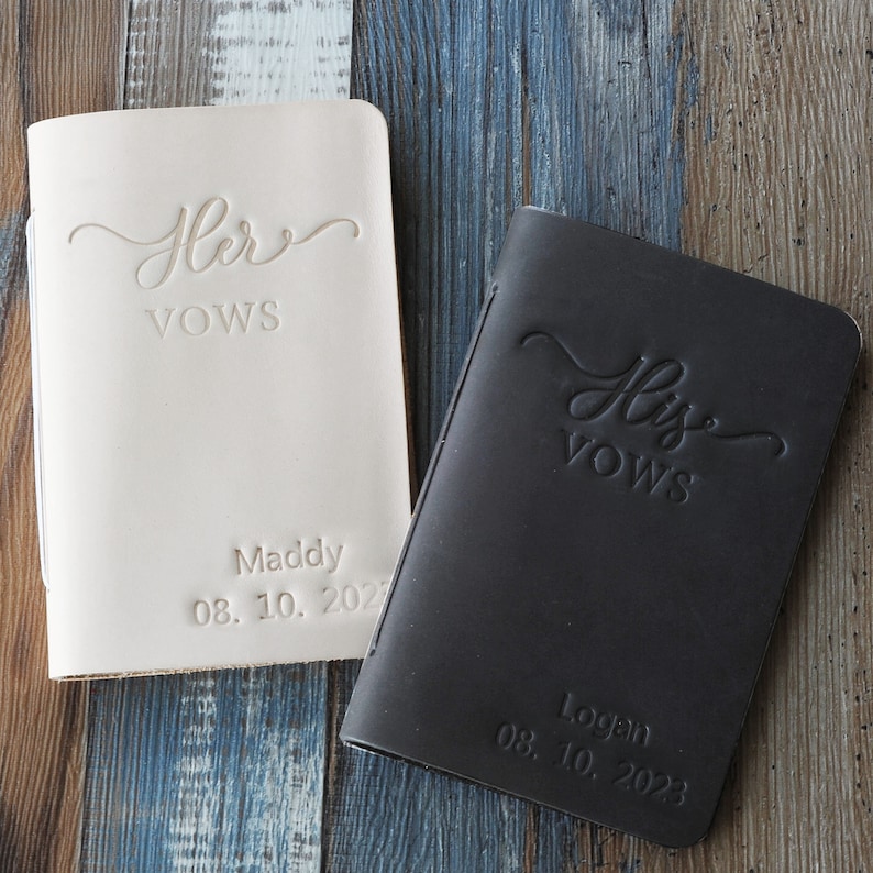 May include: Two leather-bound vow books, one in beige and one in black. The beige book has "Her Vows" and "Maddy 08.10.2023" inscribed on the front. The black book has "His Vows" and "Logan 08.10.2023" inscribed on the front.