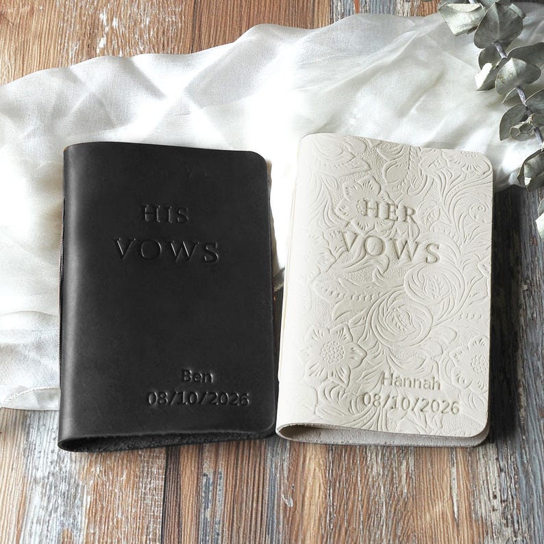 May include: Two leather vow books, one black and one cream. The black book reads "HIS VOWS" with the name "Ben" and the date "08/10/2025". The cream book reads "HER VOWS" with the name "Hannah" and the date "08/10/2026".