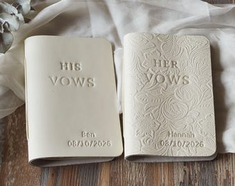 May include: Two off-white vow books. One book reads "HIS VOWS" with the name "Ben" and the date "08/10/2026". The other book reads "HER VOWS" with the name "Hannah" and the date "08/10/2026". The second book has a floral design.