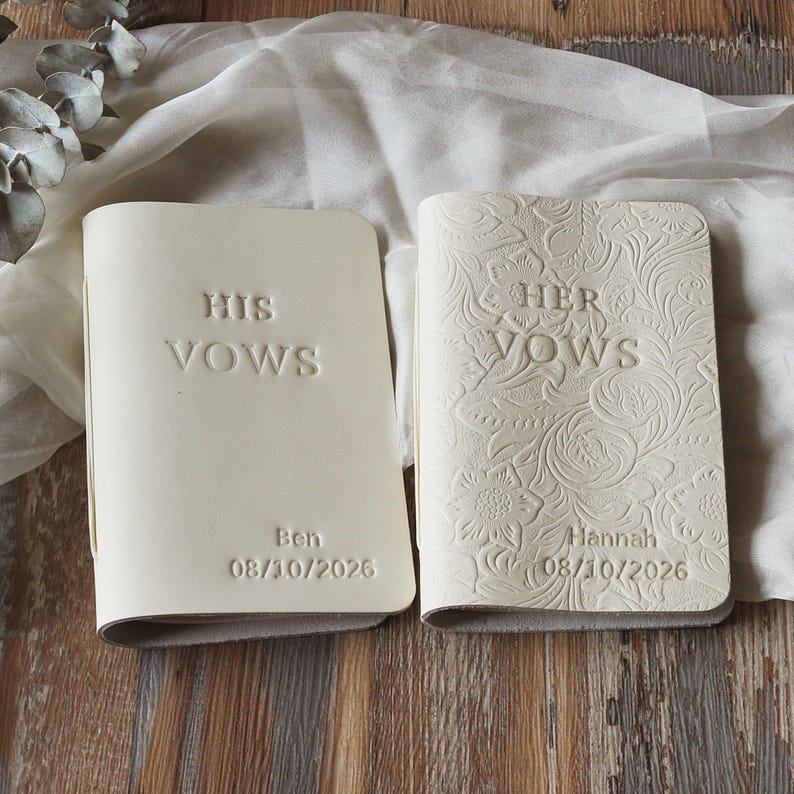 May include: Two off-white vow books. One book reads "HIS VOWS" with the name "Ben" and the date "08/10/2026". The other book reads "HER VOWS" with floral embossing, the name "Hannah" and the date "08/10/2026".
