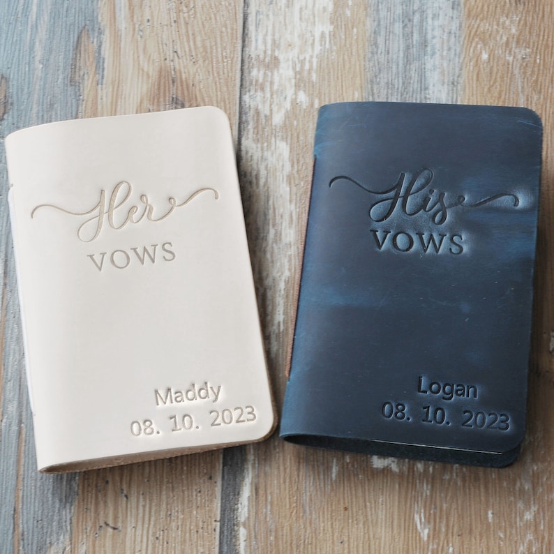 May include: Two leather-bound vow books, one white and one black, with the words "Her Vows" and "His Vows" in cursive script. The books are personalized with names and dates: "Maddy 08.10.2023" and "Logan 08.10.2023".