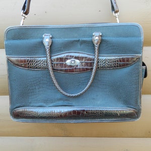 Puede incluir: Un malet&iacute;n gris oscuro con detalles en marr&oacute;n imitaci&oacute;n cocodrilo. La bolsa tiene un asa trenzada y un cierre plateado. La correa para el hombro es marr&oacute;n. El malet&iacute;n tiene un patr&oacute;n texturizado.