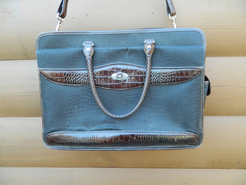 Puede incluir: Un malet&iacute;n gris oscuro con detalles en marr&oacute;n imitaci&oacute;n cocodrilo. La bolsa tiene un asa trenzada y un cierre plateado. La correa para el hombro es marr&oacute;n. El malet&iacute;n tiene un patr&oacute;n texturizado.