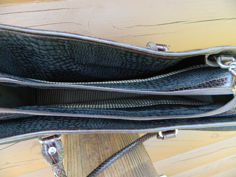 Puede incluir: Bolso de mano de cuero marr&oacute;n con m&uacute;ltiples compartimentos. El interior presenta un forro oscuro estampado y una tela a rayas. El bolso tiene un asa trenzada y herrajes plateados. El bolso est&aacute; abierto, revelando el interior.