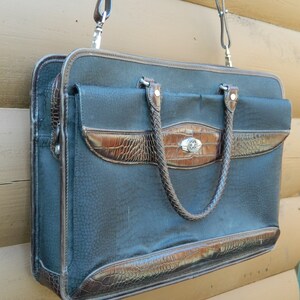 Puede incluir: Un malet&iacute;n negro con detalles en polipiel marr&oacute;n. La bolsa presenta una superficie texturizada, un asa trenzada y un cierre plateado. Incluye una bandolera y est&aacute; dise&ntilde;ada para transportar documentos y otros art&iacute;culos.