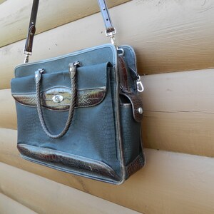 Puede incluir: Un malet&iacute;n gris oscuro con detalles en s&iacute;mil cuero marr&oacute;n. La bolsa tiene un patr&oacute;n texturizado, un asa trenzada y una correa para el hombro desmontable. El malet&iacute;n tiene un cierre plateado y un bolsillo frontal.