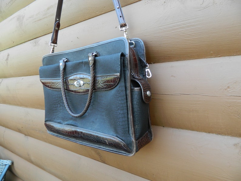 Puede incluir: Un malet&iacute;n gris oscuro con detalles en s&iacute;mil cuero marr&oacute;n. La bolsa tiene un patr&oacute;n texturizado, un asa trenzada y una correa para el hombro desmontable. El malet&iacute;n tiene un cierre plateado y un bolsillo frontal.