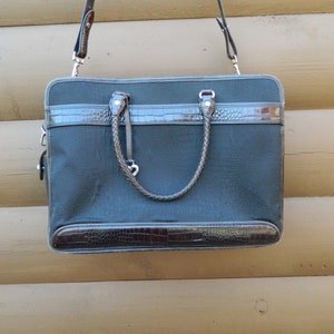 Puede incluir: Un malet&iacute;n gris oscuro con detalles en s&iacute;mil piel marr&oacute;n. La bolsa tiene un asa trenzada y una correa para el hombro desmontable. La parte superior e inferior de la bolsa tienen un dise&ntilde;o de piel de cocodrilo sint&eacute;tica.