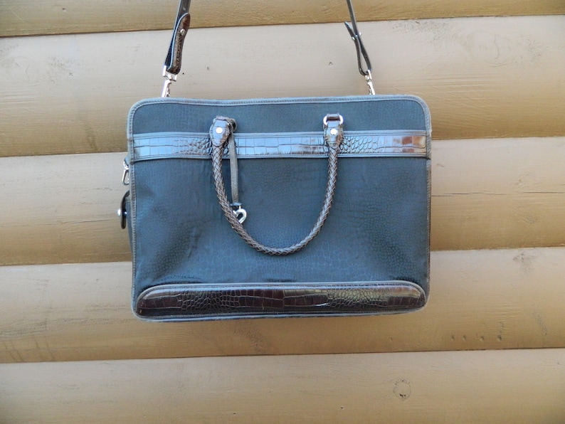 Puede incluir: Un malet&iacute;n gris oscuro con detalles en s&iacute;mil piel marr&oacute;n. La bolsa tiene un asa trenzada y una correa para el hombro desmontable. La parte superior e inferior de la bolsa tienen un dise&ntilde;o de piel de cocodrilo sint&eacute;tica.