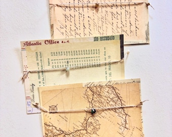 May include: Three rectangular cards featuring vintage-style prints of handwritten cursive text, a currency conversion table labeled Atlantic Office, and a detailed map. Each card is wrapped with a thin string featuring a single small bead.