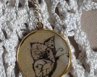 May include: A round gold-toned pendant necklace featuring a beige fabric insert with a black ink illustration of a butterfly. The pendant is suspended from a delicate gold-toned metal chain, showcasing a detailed drawing of butterfly wings.