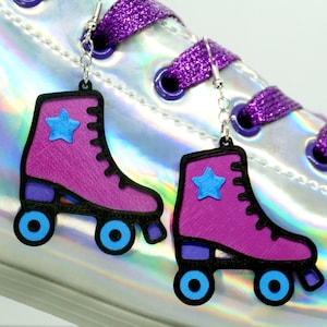 May include: Purple roller skate earrings with blue wheels and a blue star on the side. The earrings are hanging from a silver hook.