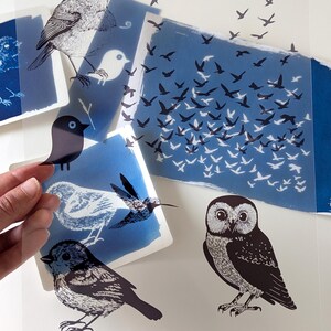 May include: A collection of bird-themed art prints featuring various bird illustrations in black and white, with blue and white backgrounds. The prints include an owl, a hummingbird, and a flock of birds in flight.