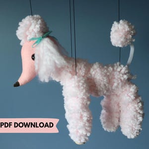 Può includere: Un burattino a forma di barboncino rosa e bianco con naso nero e fiocco turchese. Il burattino è realizzato in materiale morbido e soffice ed è sospeso da fili neri. Il testo "DIGITAL PDF DOWNLOAD" è visualizzato su uno striscione rosa.