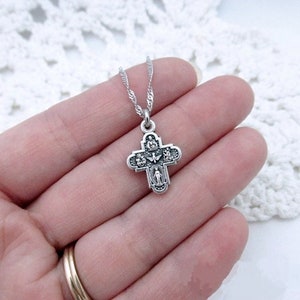 May include: Silver chain necklace with a small silver cross pendant featuring a detailed design of religious figures.