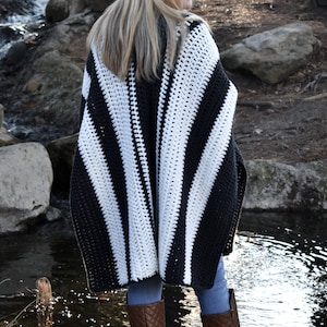 May include: A black and white striped crochet poncho. The poncho is made of thick yarn and has a geometric pattern. The person is wearing blue jeans and brown boots.