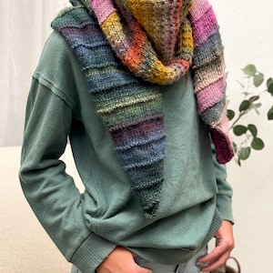 Può includere: Una sciarpa lavorata a mano, di forma triangolare, che presenta una vivace sfumatura di colori. La sciarpa comprende sfumature di blu, verde, giallo, arancione e rosa. Si indossa intorno al collo e alle spalle, aggiungendo un tocco colorato a qualsiasi outfit.